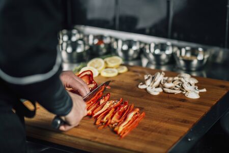 Cooking dinner in vegan restaurant. Chef holding knife and cutting red bell pepper, close-upの写真素材
