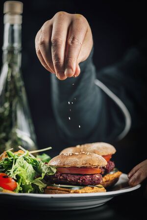 Male cook in a restaurant, decorating vegan burger with falling sesame. の写真素材