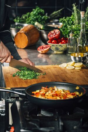 Chef holding knife, cutting parsley on wooden cutting board in vegan restaurantの写真素材