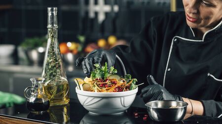 Female chef in restaurant decorating salad with parsley.