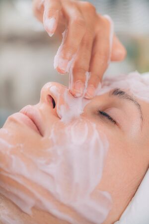 Applying face calming mask on beautiful womanâ€™s face. Shaken protein mousse.