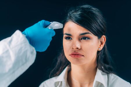 Coronavirus. Medical worker in hazmat protective suite checking body temperature, woman with...
