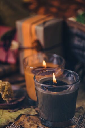 Scented brown and orange candles with presents, dried flowers and leaf decoration on table. Copy spaceの写真素材