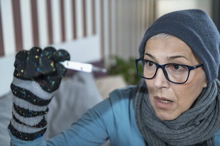 Mature woman with fever looking at Digital Thermometer for Body Temperature