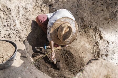 Female archaeologist digging up ancient pottery object at an archaeological site.の写真素材