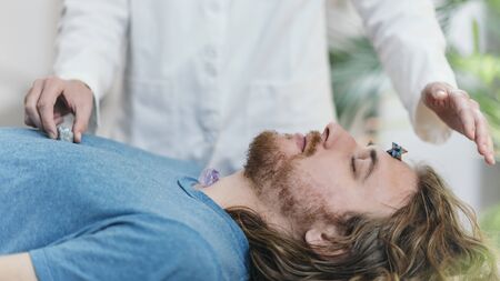 Chakra Therapy with Crystals. Young man lying on massage table, having chakra healing treatment