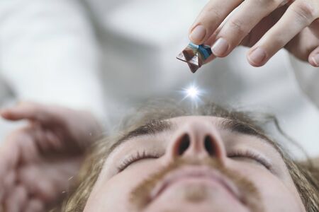 Healing crystal. Young man with Merkaba crystal placed on his forehead on third eye's area. 