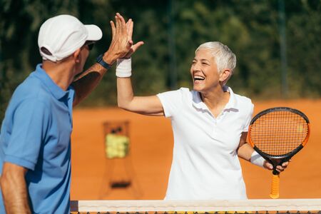 Tennis Coach Practicing Service with Senior Woman on Outdoor Tennis Class. Giving high five.の写真素材