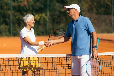 Tennis Instructor with Senior Woman in her 60s Handshaking after Having a Tennis Lesson on Clay Court.の写真素材