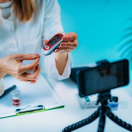Telemedicine â Medical doctor having a virtual conference session with patient and demonstrating how to measure blood sugarの写真素材