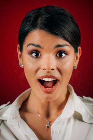 Emotion Surprise. Beautiful young woman feeling surprised or expressing surprise, studio portrait, red backgroundの写真素材