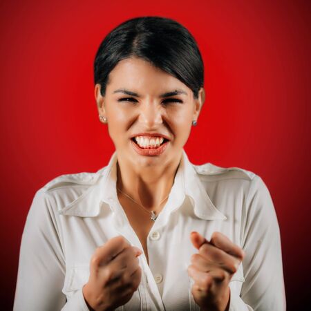 Emotion Anger. Face of a angry young woman, expressing anger, studio portrait, red backgroundの写真素材