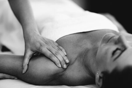 Physiotherapist massaging female patient with injured shoulder.  Sports injury treatment.の写真素材
