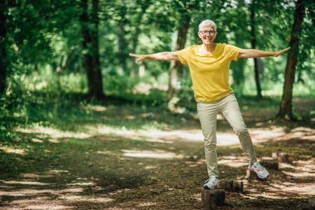 Balancing exercise outdoors. Mature woman standing on one leg, exercising balanceの写真素材