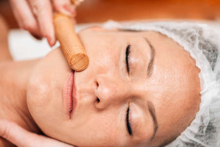 Maderotherapy face massage. Massaging woman's face with wooden double roller massagerの写真素材