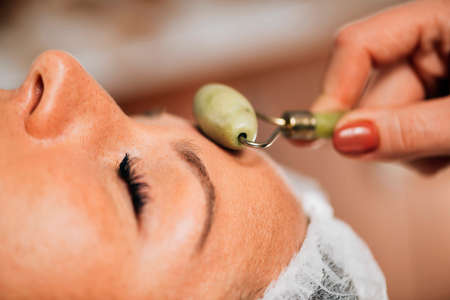 Maderotherapy face massage. Massaging woman's face with wooden double roller massagerの写真素材