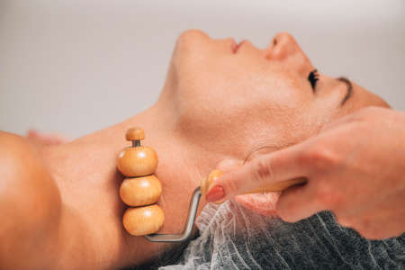 Maderotherapy face massage. Massaging woman's face with wooden double roller massagerの写真素材