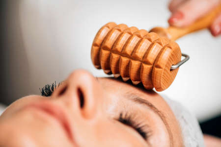 Maderotherapy face massage. Massaging woman's face with wooden double roller massagerの写真素材