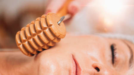 Maderotherapy face massage. Massaging woman's face with wooden double roller massagerの写真素材