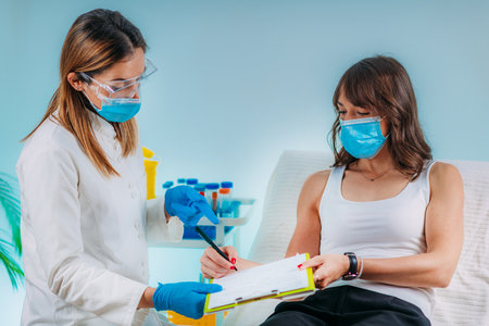 Nurse with Protective Mask Filling in Information Form. Blood Drawing and Analysis During Covid19 Coronavirus Crisisの写真素材