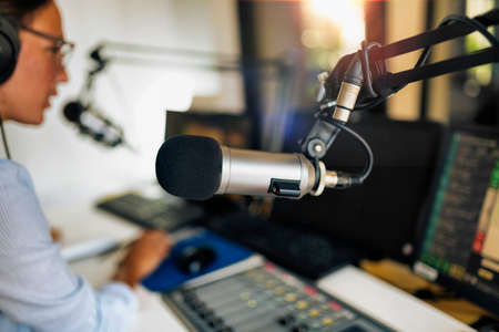 Microphone in a podcasting studio, young host and the broadcasting equipment in the background