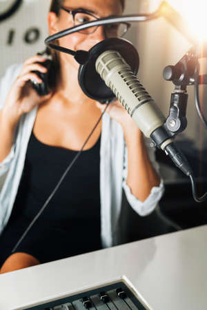 Attractive young millennial woman in front of microphone, using headphones, making an online radio podcast talk show.の写真素材