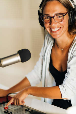 Attractive young millennial woman in front of microphone, using headphones, making an online radio podcast talk show.の写真素材