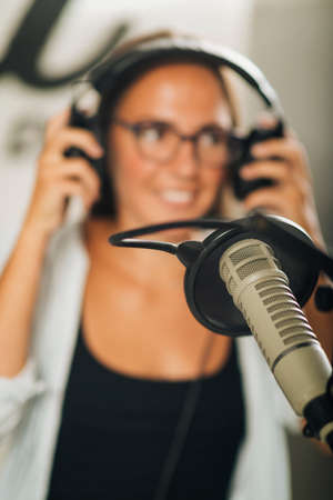 Attractive young millennial woman in front of microphone, using headphones, making an online radio podcast talk show.の写真素材