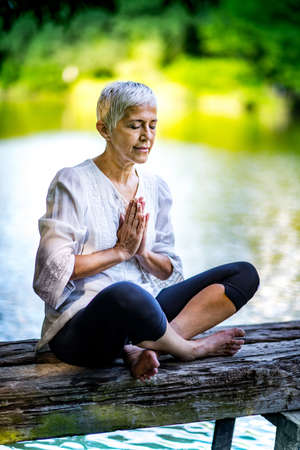 Beautiful mindful senior woman meditating by the waterの写真素材