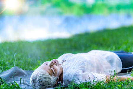 Mindful mature woman meditating by the water, lying down, feeling connected to the earth and natureの写真素材