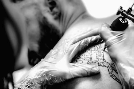 Female tattoo artist prepares tattoo machine for making a tattoo on a menâs armの写真素材