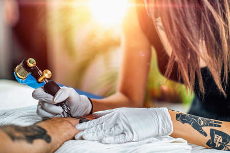 Tattooing safety during coronavirus crisis. Tattoo artist tattooing client with gloves and face mask in a tattoo studio during COVID-19 pandemicの写真素材