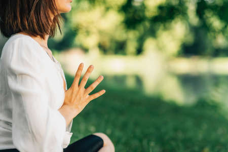 Tranquility. Peaceful young women sitting in lotus pose meditating by the Water. Keeping hands...