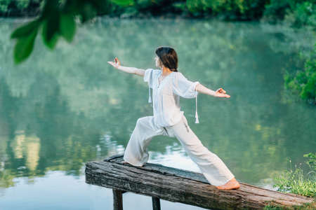 Yoga by the Lake - Young woman practicing Warrior 2 Pose or Virabhadrasana IIの写真素材