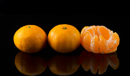 Ripe tangerines on black background with reflectionの写真素材