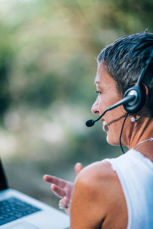 Remote work. Positive middle-aged woman working remotely, wearing a headset, talking