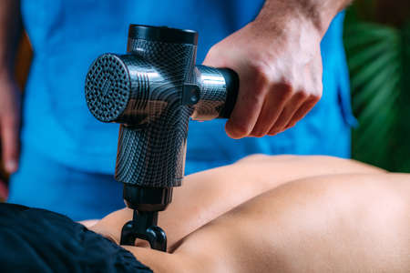 Physiotherapy Therapist Treating Lower Back on Athlete with Massage Gun with Fork Headの写真素材