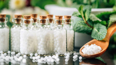 Homeopathy Concept. Homeopathic globules spilled around, wooden spoon filled with homeopathic pills,...