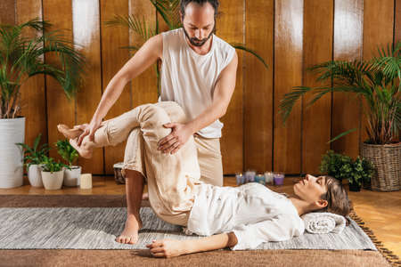 Traditional Thai Yoga Passive Stretching Relaxing Technique. Young woman enjoying benefits of passive stretching  leg techniqueの写真素材