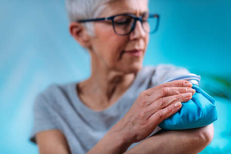 Elbow pain treatment. Senior woman holding an ice bag compress on a painful elbowの写真素材