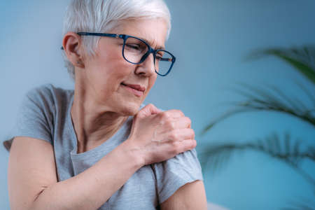 Frozen shoulder. Senior woman holding cold compress, ice bag pack on her painful shoulderの写真素材