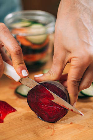 Fermentation process. Woman preparing vegetables for fermentation at home. Cutting cucumber and beets.の写真素材