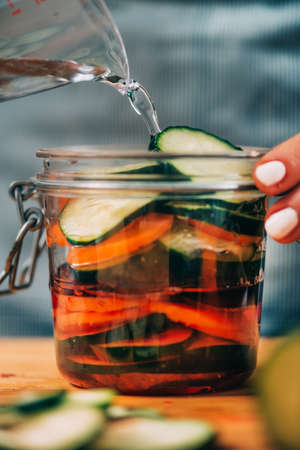 Homemade fermented vegetables. Woman pouring water in the jar with vegetables. Vegetable...