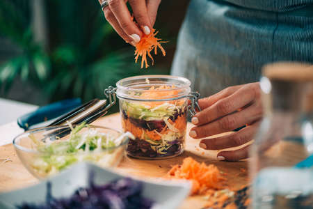 Fermenting vegetables. Woman putting cabbage and carrots in the jar, preparing them for fermentation.の写真素材