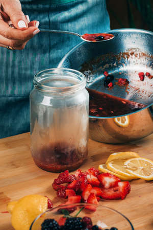 Fruit canning at home. Woman pouring cooked jam into sterile jars. Fruit preservation.