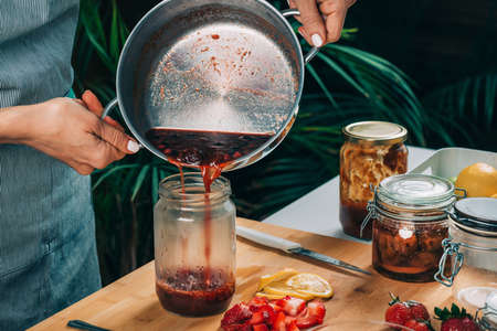 Fruit canning at home. Woman pouring cooked jam into sterile jars. Fruit preservation.の写真素材
