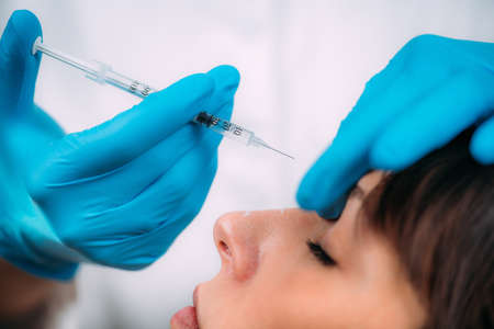 Dermal filler injection treatment. Doctor with surgical gloves injecting dermal filler into womenâs nose bridge.の写真素材