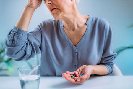 Senior woman with migraine headache holding painkiller pillsの写真素材