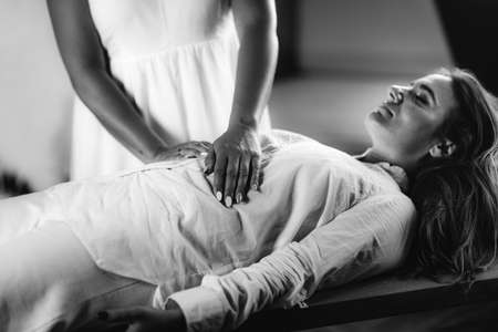 Female Therapist Performing Reiki Therapy Treatment. Hands Over Woman's Stomach. Alternative Therapy Concept, Stress Reduction and Relaxation.の写真素材