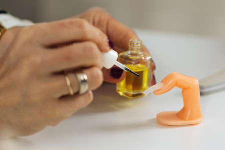Manicure and nail technician course and training. Beautician applying cuticle oil on nails and...